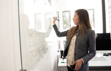 Woman Wearing Gray Blazer Writing on Dry-erase Board